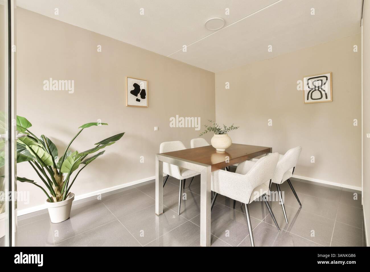 Un'elegante zona pranzo con un tavolo alla moda, sedie contemporanee, pareti decorative e una pianta che creano un ambiente caldo e invitante. Foto Stock