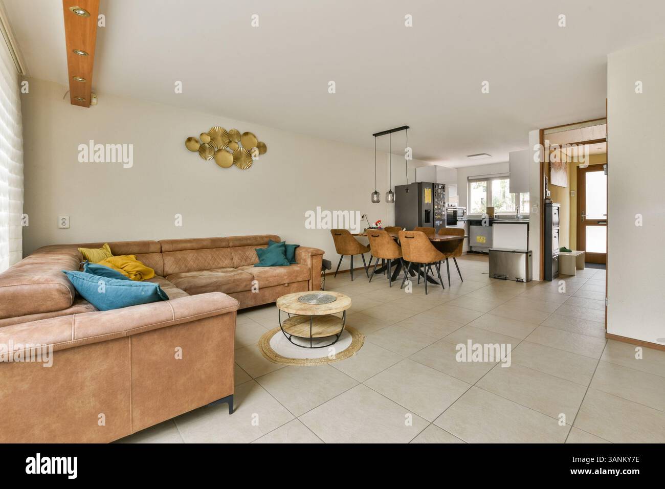 Un elegante e moderno soggiorno con un comodo divano marrone, pareti decorative e una funzionale zona pranzo che mette in mostra elementi di design contemporaneo. Foto Stock