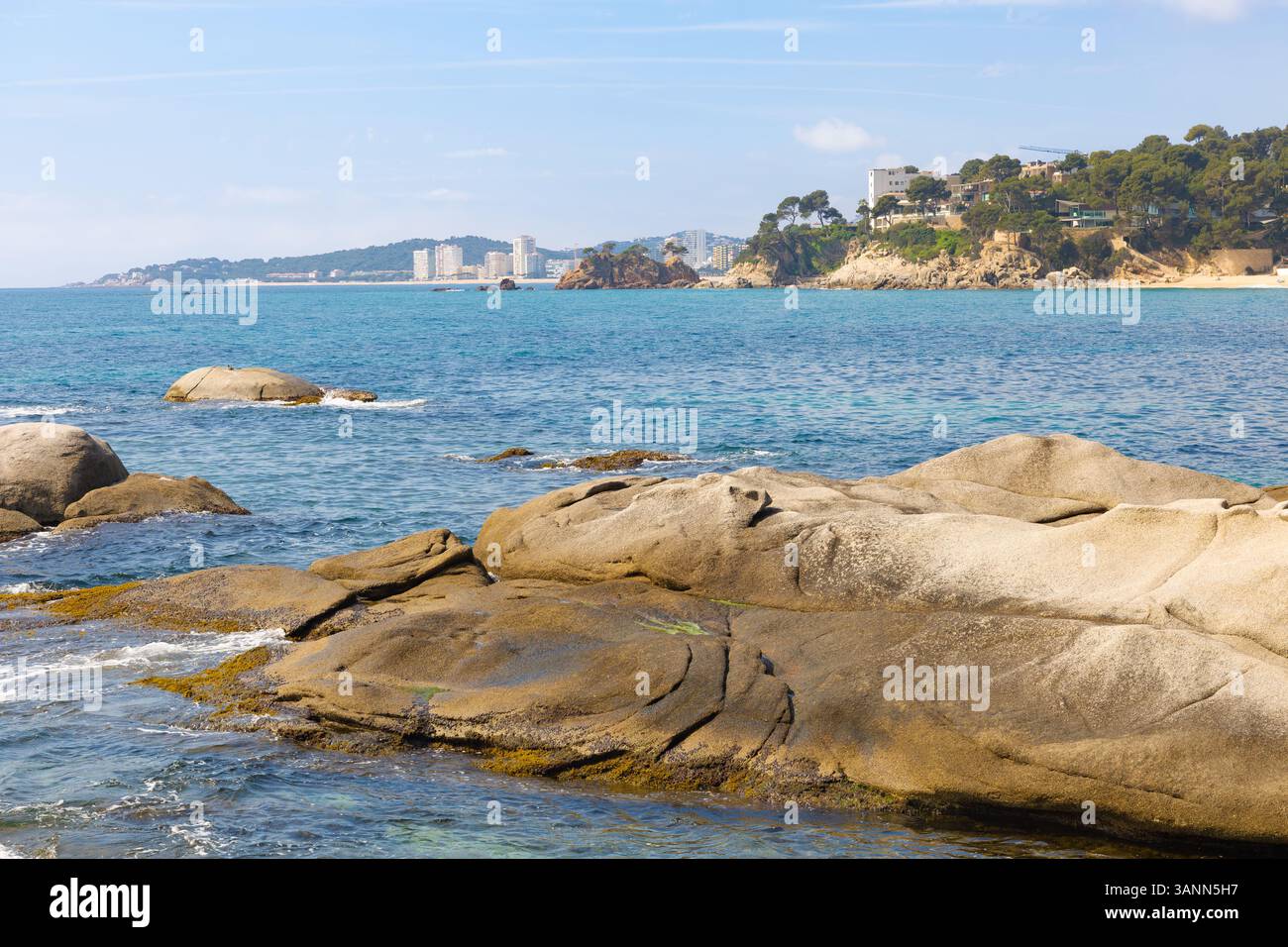 Le lisce rocce in primo piano a Punta Rocas Planes incorniciano il blu del Mar Mediterraneo e la lontana vista della costa verso Platja d'Aro, Costa Brava. Foto Stock