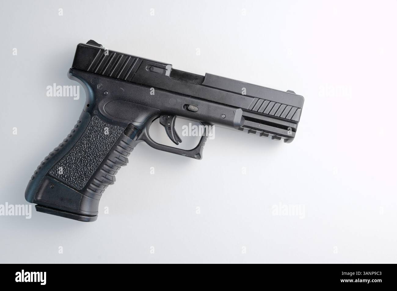 Un'elegante pistola nera si appoggia su una superficie bianca incontaminata, evidenziandone il design elegante e le caratteristiche distintive Foto Stock