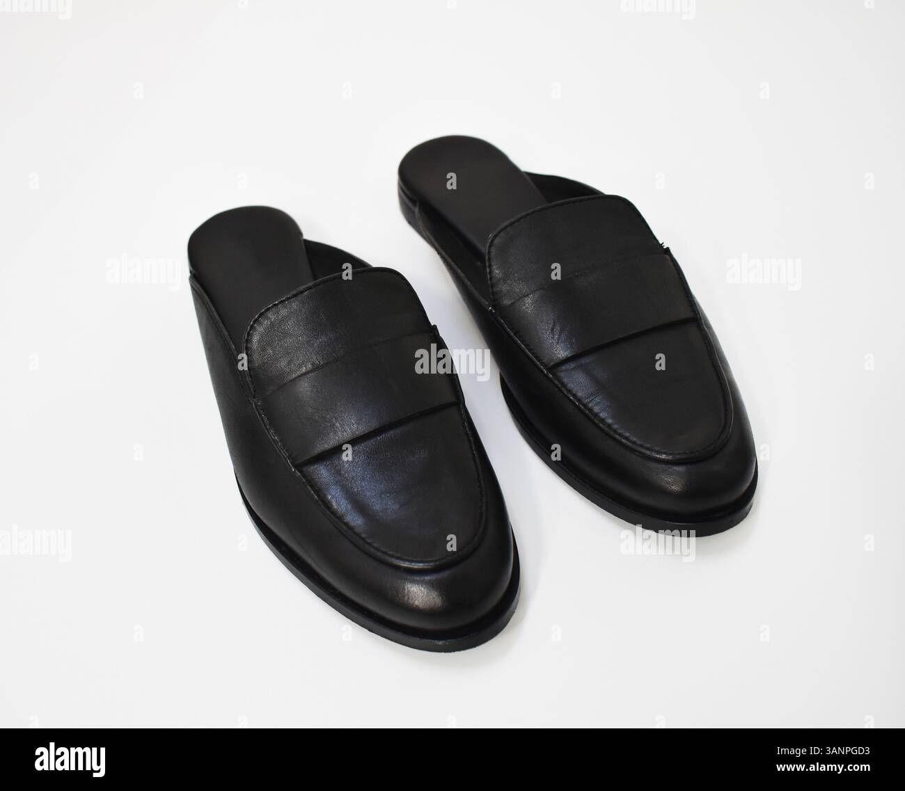 scarpe slide da donna in pelle nera con suola grossa, moderni mocassini a forma di mulo su superficie bianca, scarpa primaverile essenziale per l'abbigliamento casual e da ufficio Foto Stock