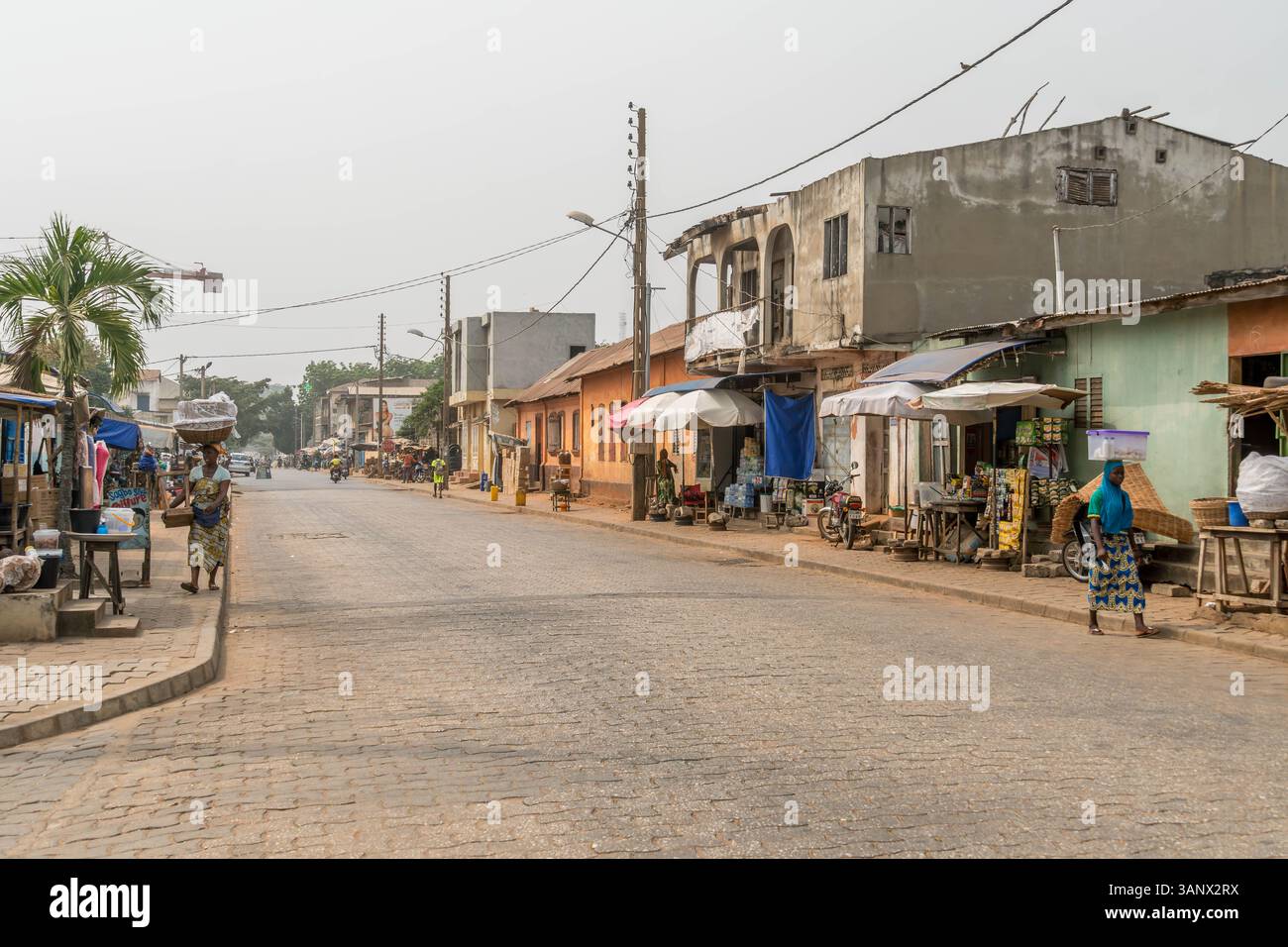 La capitale del Benin, Porto-Novo, con strade povere e bancarelle del mercato, gente africana locale che cammina e una motocicletta. Foto Stock