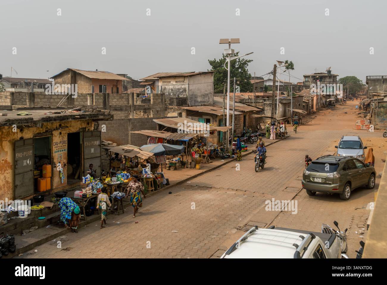 Quartieri poveri e polverosa via Porto-Novo con vecchi edifici, zona povera con bancarelle del mercato e residenti locali del Benin, Africa occidentale. Foto Stock