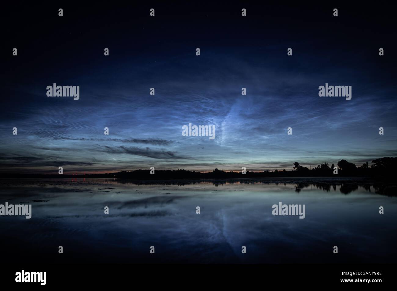 Una vista serena delle nuvole nocciolenti che si illuminano dolcemente sopra un lago fermo durante il crepuscolo. Le sfumature blu del cielo si riflettono sull'acqua calma Foto Stock