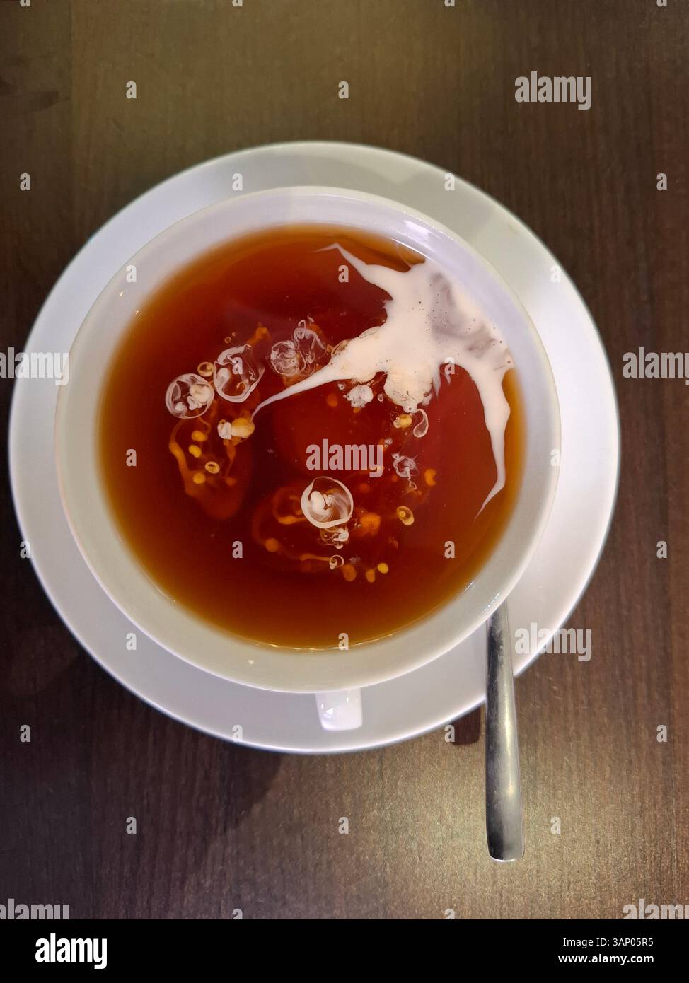 La panna di caffè viene versata in una tazza di tè bianco e si mescola con il tè in modo torbido. Foto Stock