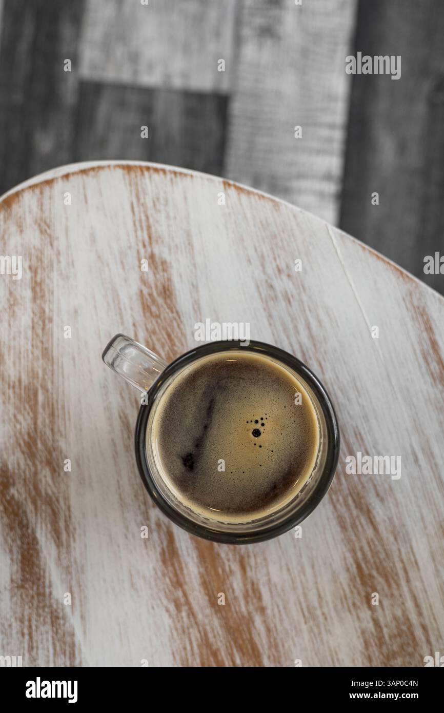 Una tazza da caffè calda poggia su un tavolo di legno con ricche texture che mescolano sfumature bianche e marrone miele, creando un'atmosfera rustica ed elegante. Foto Stock