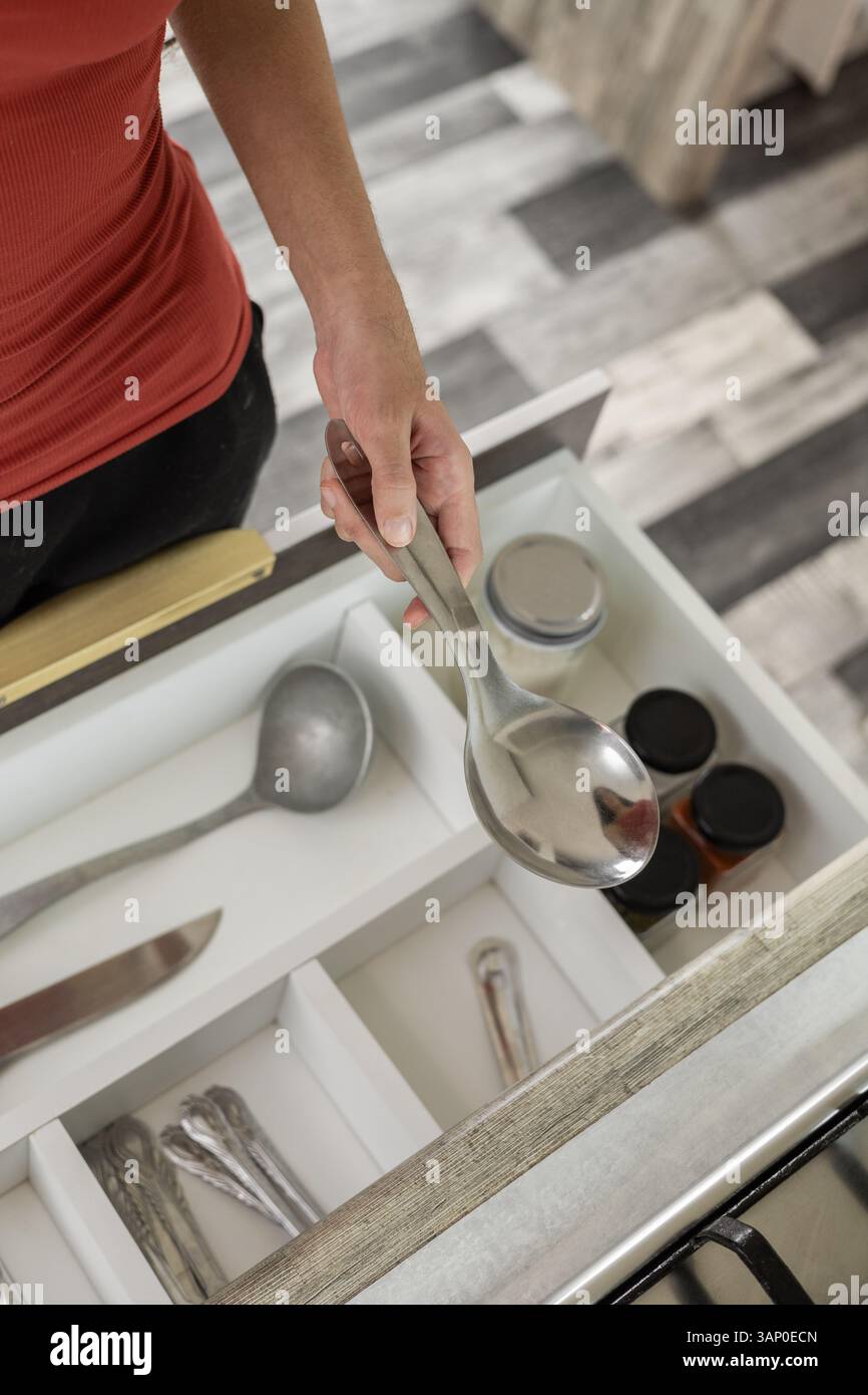 Una prospettiva alternativa di un cassetto aperto che rivela utensili da cucina organizzati, come cucchiai, mestoli, coltelli, forchette e altro ancora, all'interno di un'elegante e moderna cabina in legno Foto Stock