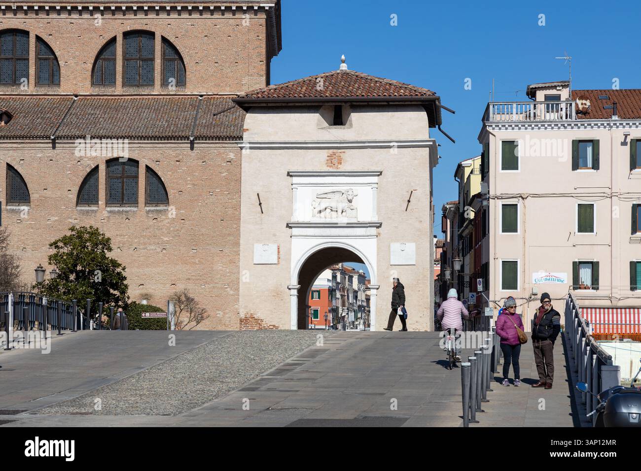 Chioggia, Italia - 3 marzo 2025: Porta Garibaldi e il Duomo, con persone che camminano e pedalano nel centro storico della città Foto Stock