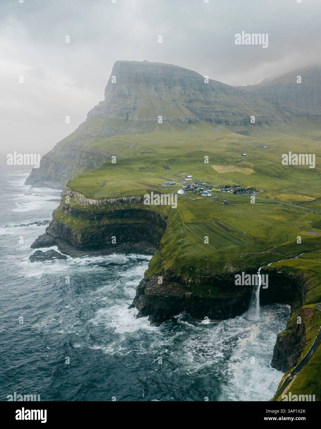 Vista aerea del pittoresco villaggio di Gasadalur con una splendida cascata che si getta da un'aspra scogliera nell'oceano, Vagar, Isole Faroe. Foto Stock