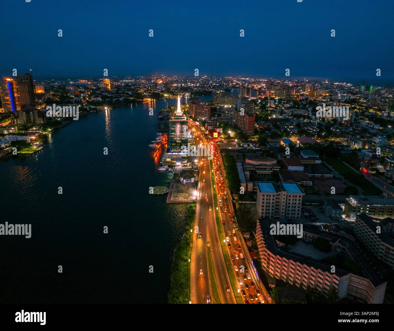 Veduta aerea del vivace paesaggio urbano con grattacieli illuminati e traffico intenso lungo il fiume, Lagos, Nigeria. Foto Stock