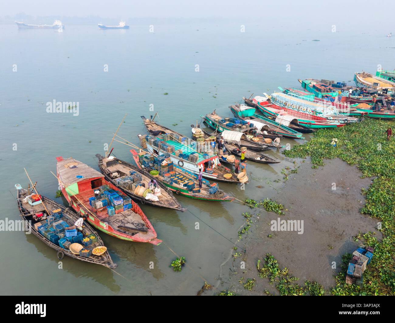 Vista aerea di un mercato invernale con cesti di verdure e barche da pesca lungo un tranquillo fiume, Brahmanbaria, Bangladesh. Foto Stock