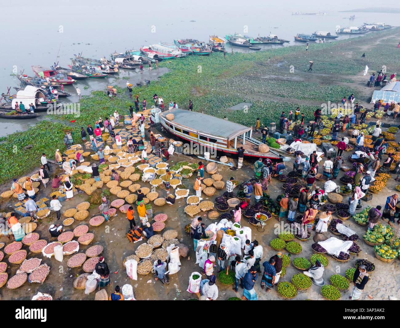 Vista aerea di un vivace mercato invernale con cesti di verdure e barche lungo il fiume, Brahmanbaria, Bangladesh. Foto Stock