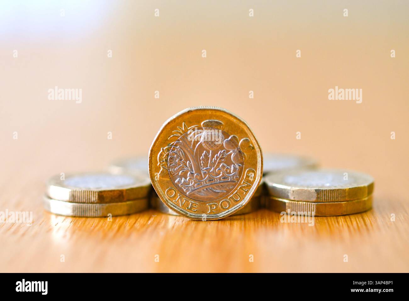 Una sola moneta inglese da una sterlina in piedi sul bordo di una scrivania con altre monete distese Foto Stock