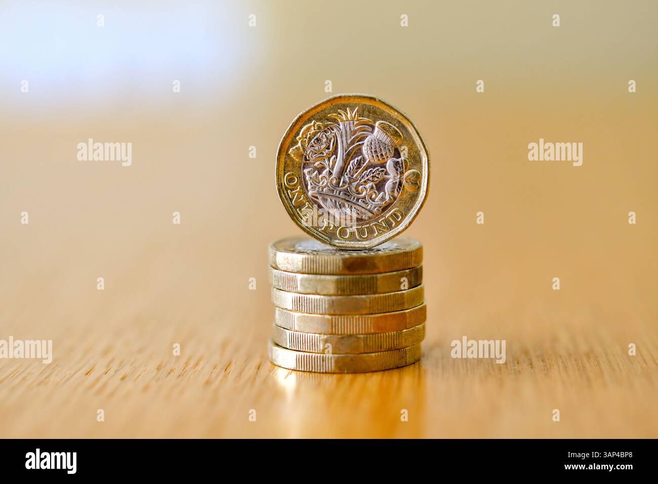 Una sola moneta britannica da una sterlina sul bordo di una scrivania con altre monete distese su uno sfondo defocalizzato Foto Stock