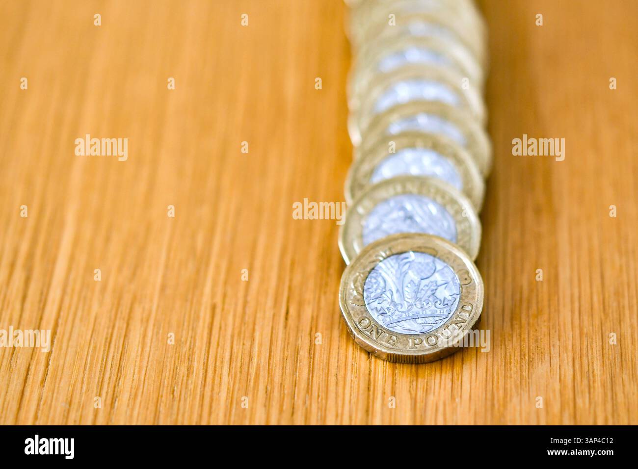 Una sola moneta britannica da una sterlina appoggiata su una colonna di monete da una sterlina su una scrivania Foto Stock