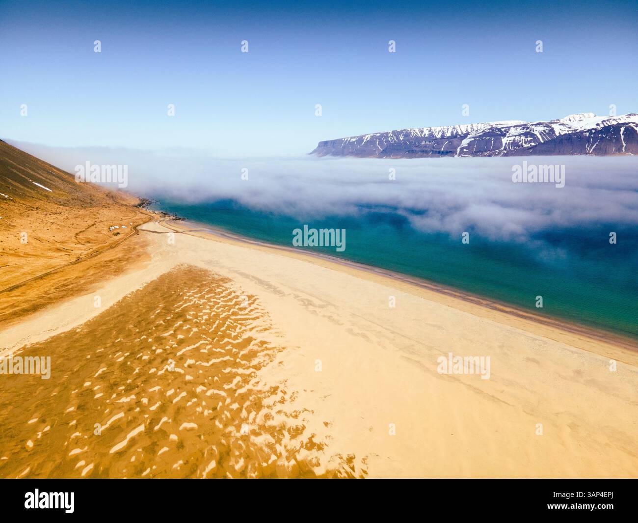 Vista aerea di un tranquillo fiordo avvolto dalla nebbia con una splendida spiaggia e montagne maestose, Bildudalur, Islanda. Foto Stock
