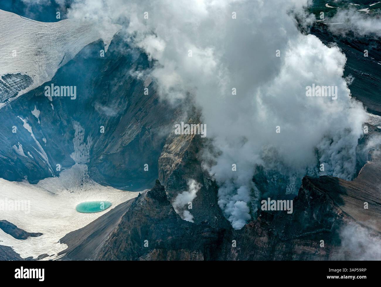 Vista aerea del vulcano Gorely con fumo che sale dal cratere, circondato da terreni accidentati innevati, penisola di Kamchatka, Russia. Foto Stock