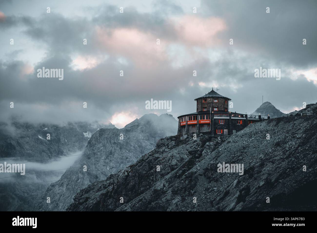 Stelvio, Italia - 29 giugno 2022: Veduta aerea delle maestose dolomiti con una cabina tranquilla tra cime rocciose e cielo nuvoloso, Stelvio, Italia. Foto Stock