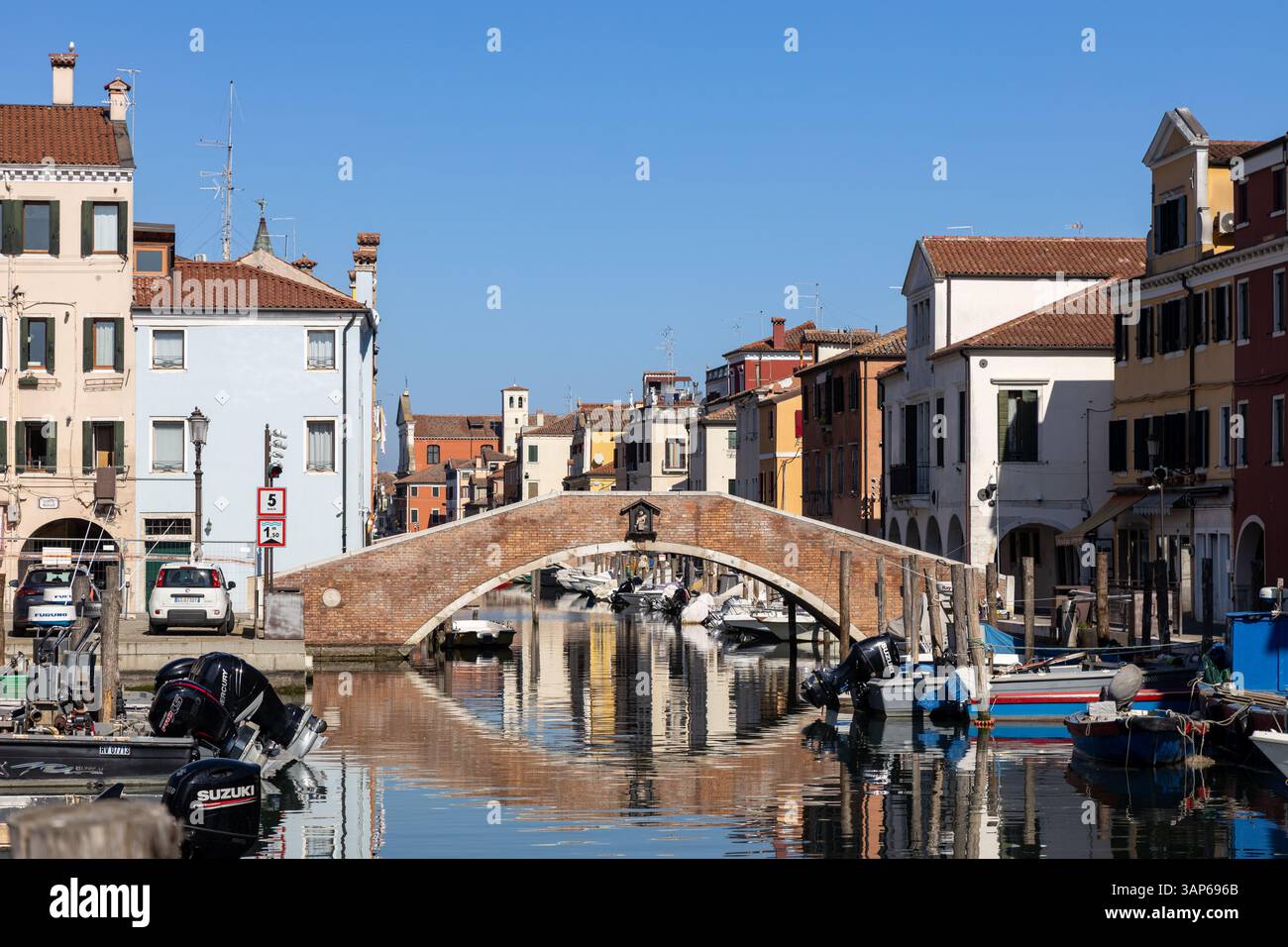 Chioggia, Italia - 3 marzo 2025: Ponte in mattoni sul Canal Vena con barche ormeggiate ed edifici colorati nel centro storico Foto Stock