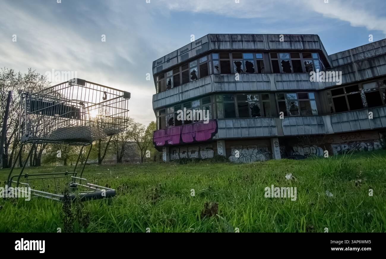 Carrello scartato di fronte al DDR Sporthotel abbandonato a Berlino-Hohenschönhausen al tramonto. Foto Stock