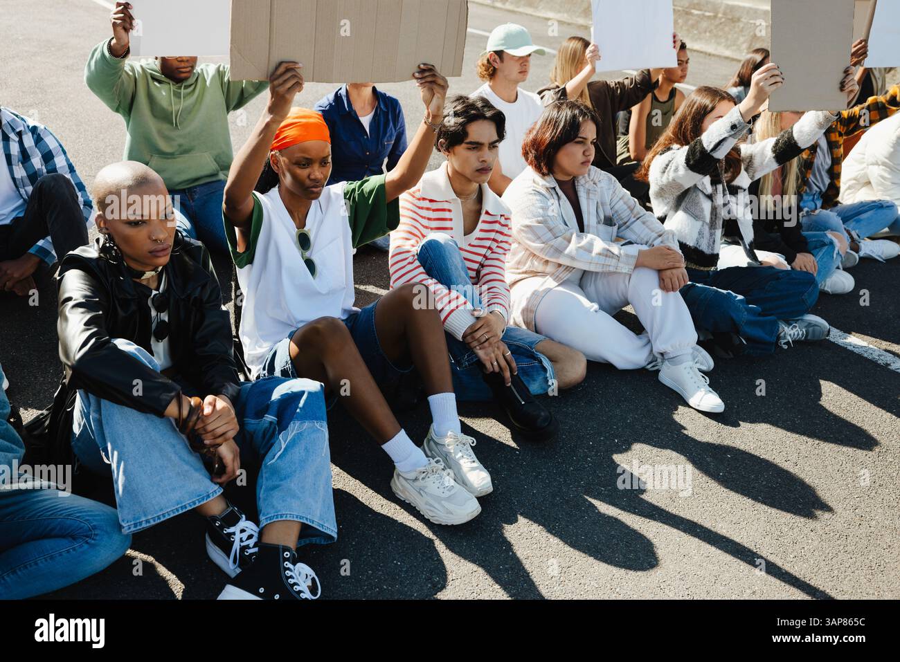 Un gruppo di individui di diversa provenienza seduti insieme tenendo cartelli bianchi, partecipando a una pacifica protesta all'aperto, esprimendo la loro u Foto Stock