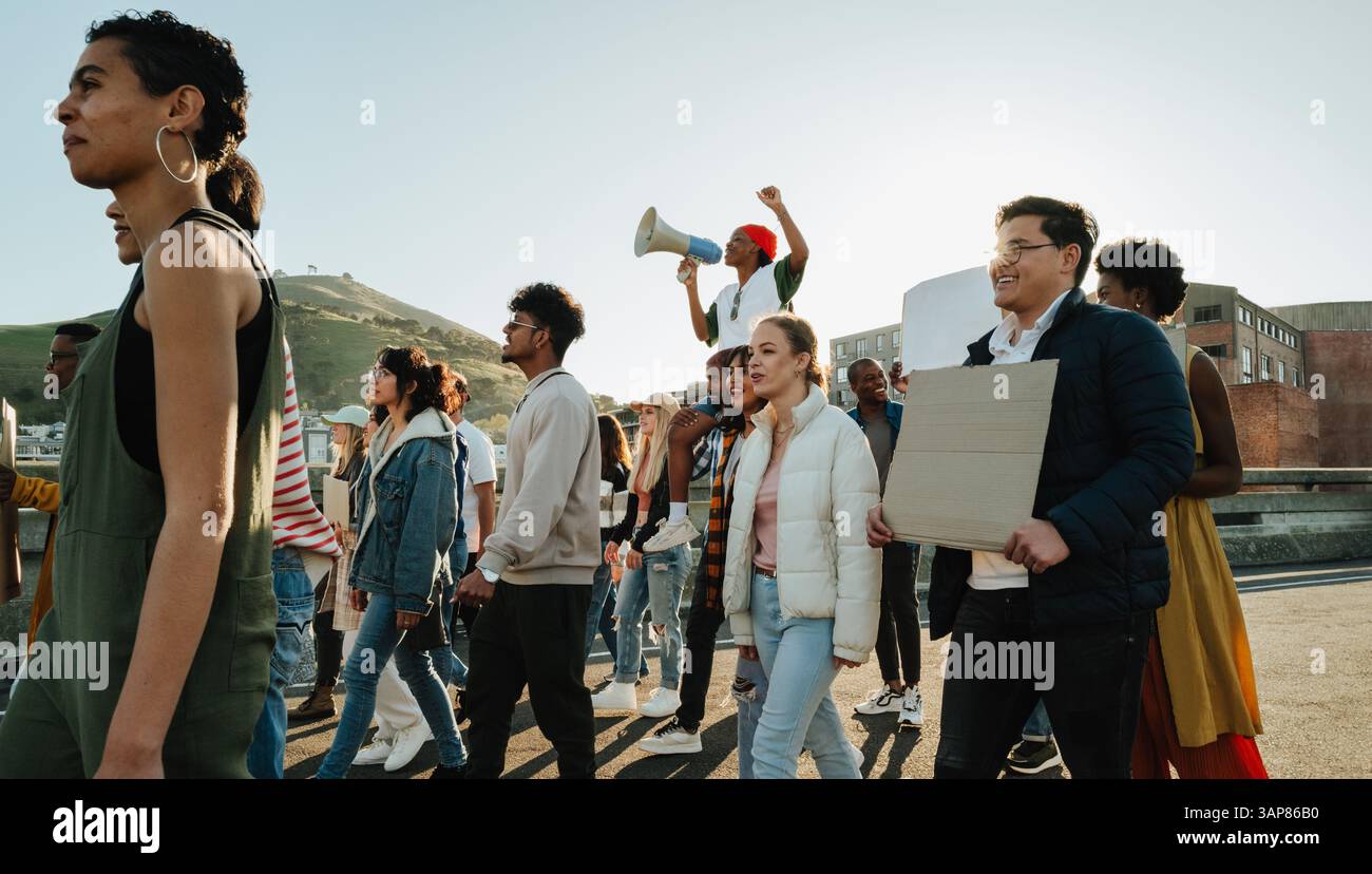 Un gruppo misto di persone che partecipano a una protesta pubblica, tenendo dei cartelli e cantando per esprimere le credenze condivise in un ambiente urbano all'aperto Foto Stock