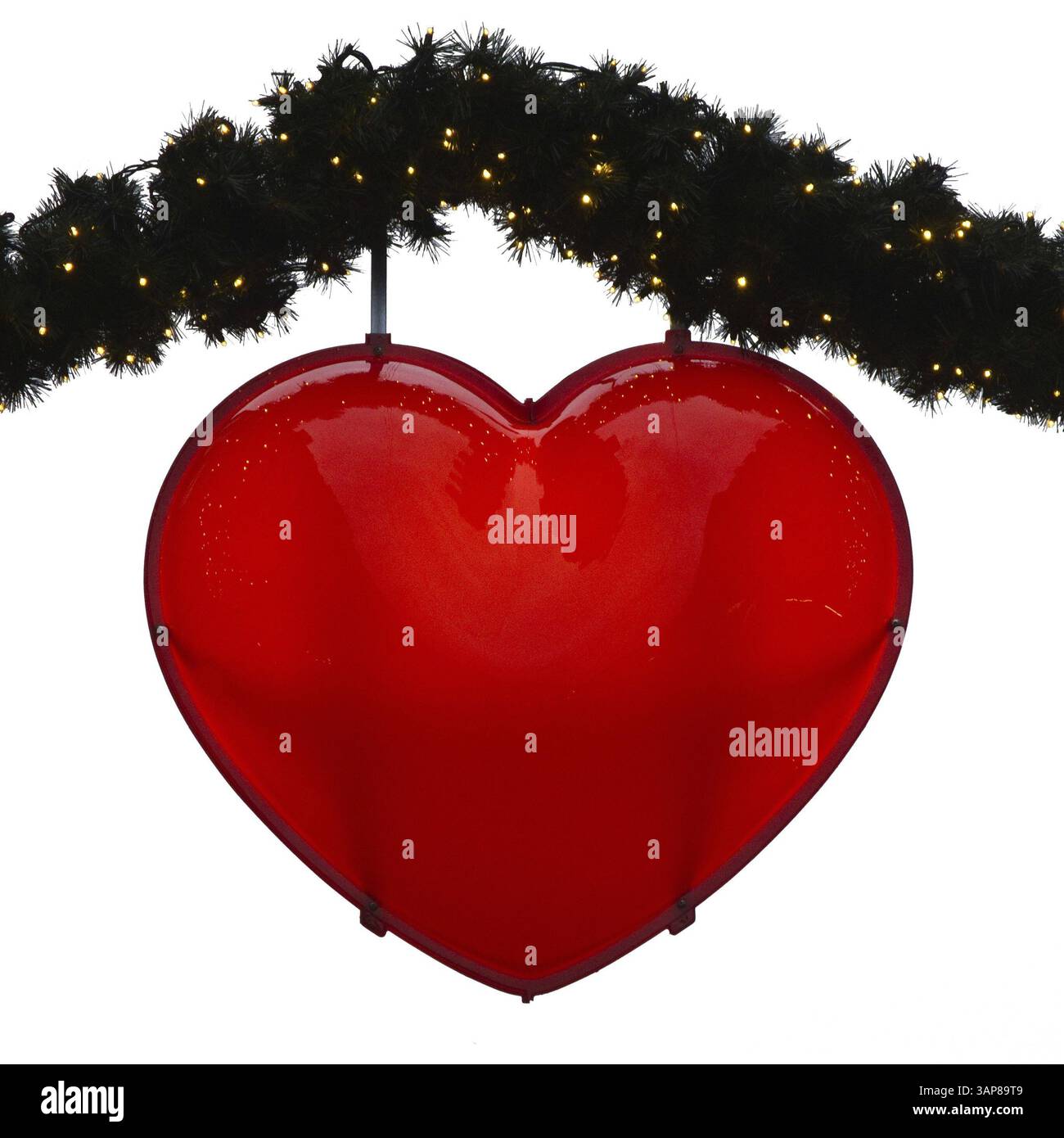 Cuore rosso collegato a rami verdi con piccole luci su terreno bianco Foto Stock