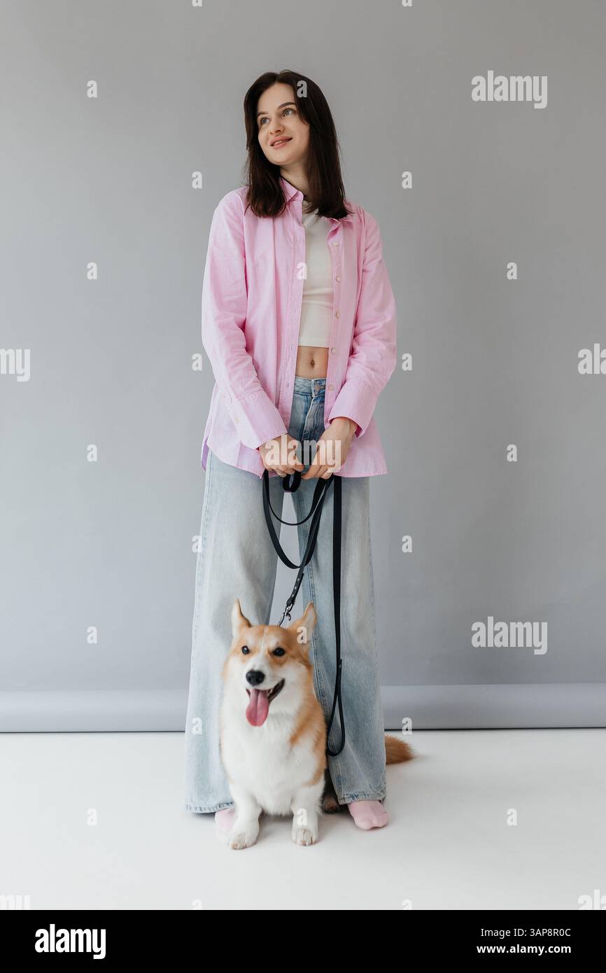 Una giovane donna elegante e alla moda posa con fiducia con il suo adorabile cane Corgi, mostrando un senso di stile moderno in un'atmosfera artistica e vivace Foto Stock