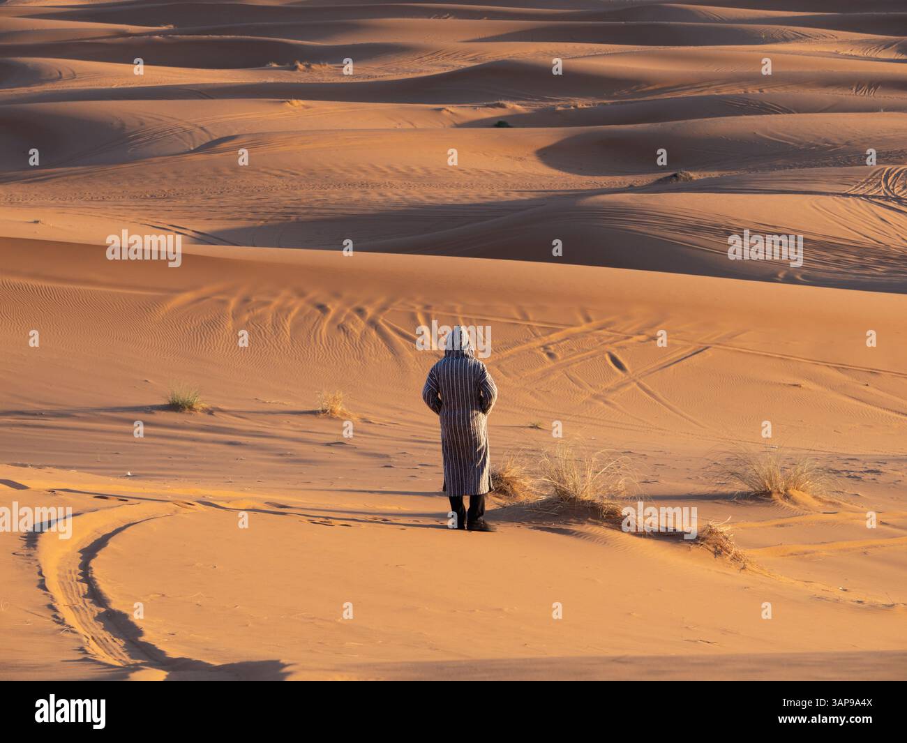 Camminare nel Sahara: Un beduino attraverso l'infinito deserto in abbigliamento tradizionale Foto Stock