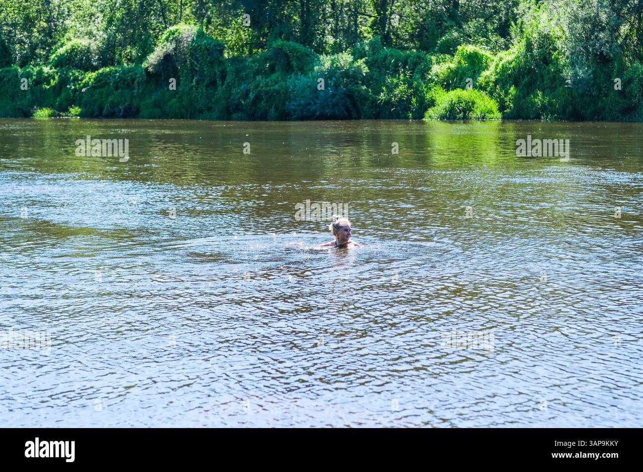 Un uomo sta nuotando in un lago. L'acqua è calma e limpida. Quell'uomo indossa un costume da bagno Foto Stock