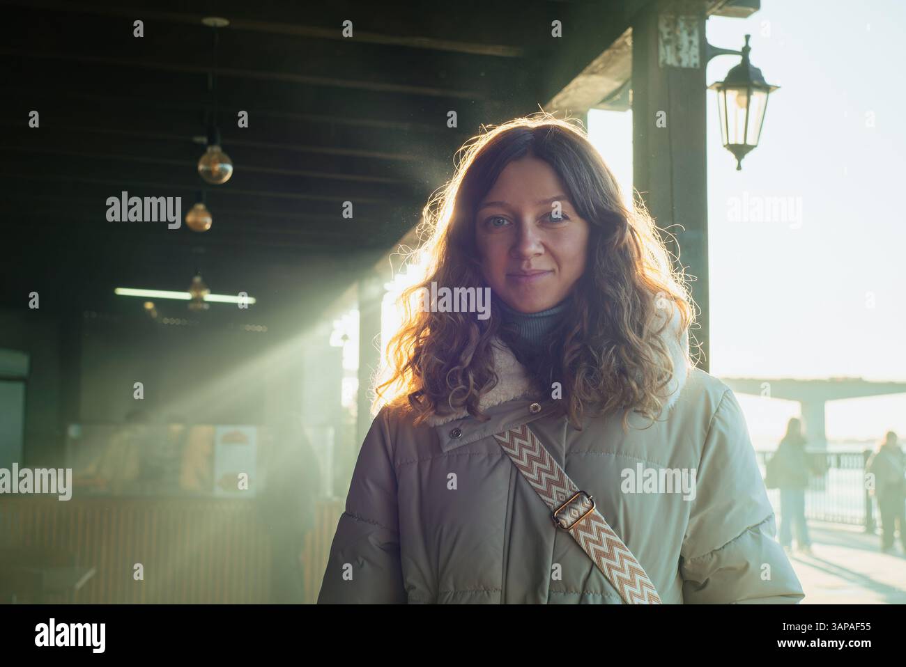 La giovane donna che indossa un caldo cappotto invernale sorride in un raggio di luce al mercato di rialto a venezia, in italia, con la luce del sole dorata che le illumina i capelli ricci Foto Stock