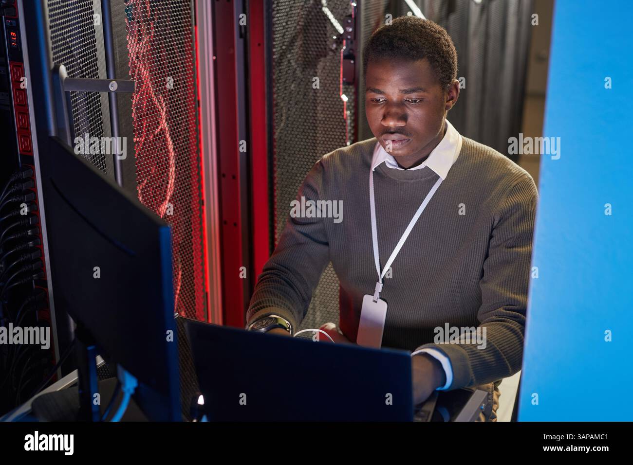 Ritratto di un tecnico IT dedicato che si concentra sulle sue attività nella sala server, circondato da tecnologia e server, a dimostrazione dell'impegno per la sua professione Foto Stock