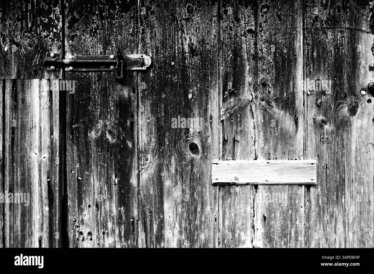 Una porta in legno resistente agli agenti atmosferici, fissata con un bullone arrugginito e rinforzata con un rinforzo in legno improvvisato, rappresenta una testimonianza del tempo e degli elementi. La d Foto Stock