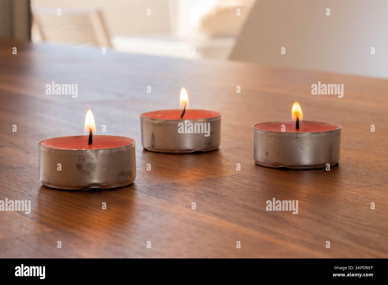 Tre candele da tè accese sul tavolo di legno Foto Stock