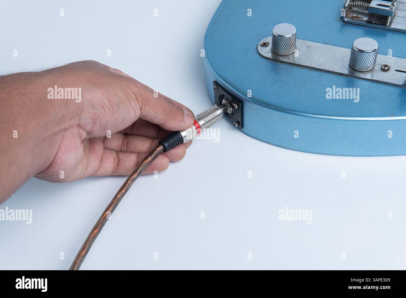 Primo piano di una mano che inserisce un cavo audio nel corpo di una chitarra elettrica blu. Isolato su sfondo bianco. Foto Stock