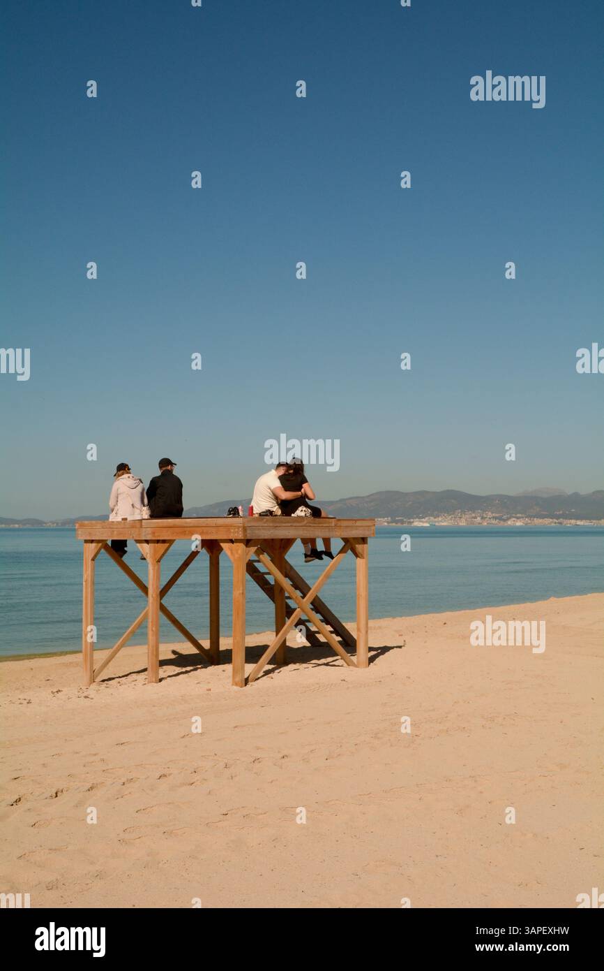 Due coppie si sono sedute su una piattaforma bagnino sulla spiaggia di Les Meravelles, Maiorca, Spagna. Palma di Maiorca può essere vista dall'altra parte della baia di Palma Foto Stock