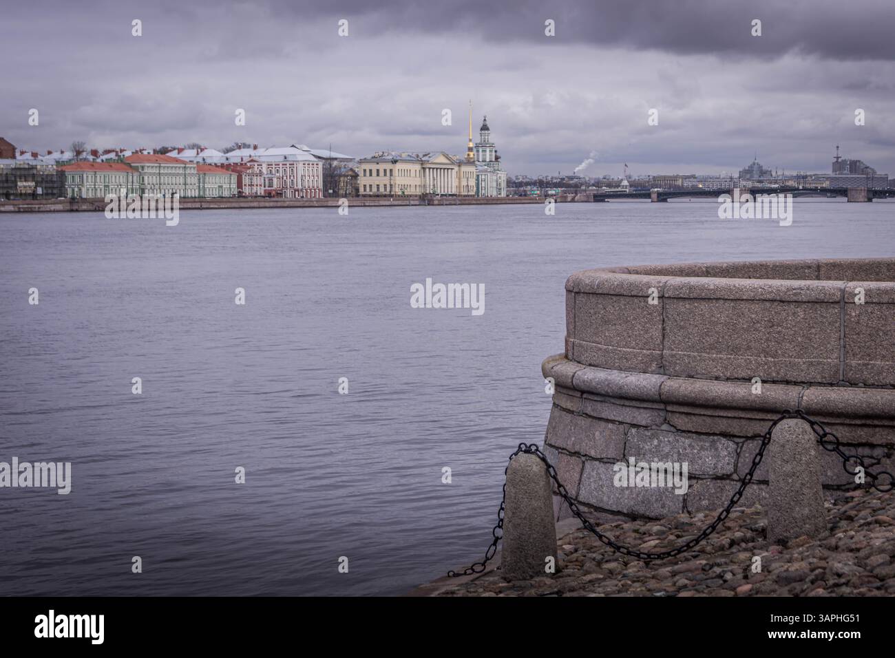 Vista di San Pietroburgo dall'isola Vasilevsky, con il fiume Neva, e l'architettura storica sotto il cielo nuvoloso, e argini in pietra in primo piano. Foto Stock