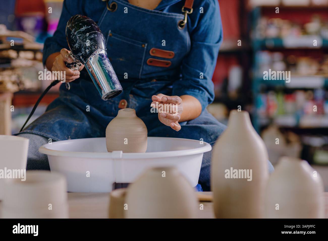 Una giovane donna messicana di 24 anni usa un asciugacapelli per asciugare un pezzo di ceramica. Il primo piano mette in evidenza la precisione e la cura che ha nelle mani durante il processo. Foto Stock