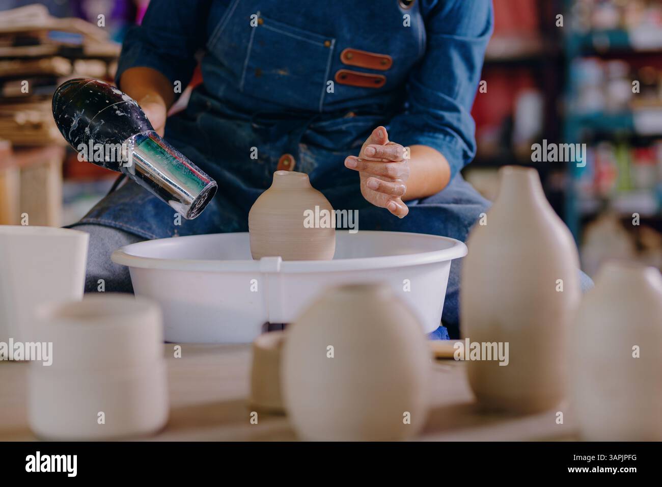 Una giovane donna messicana di 24 anni usa un asciugacapelli per asciugare un pezzo di ceramica. Il primo piano mette in evidenza la precisione e la cura che ha nelle mani durante il processo. Foto Stock