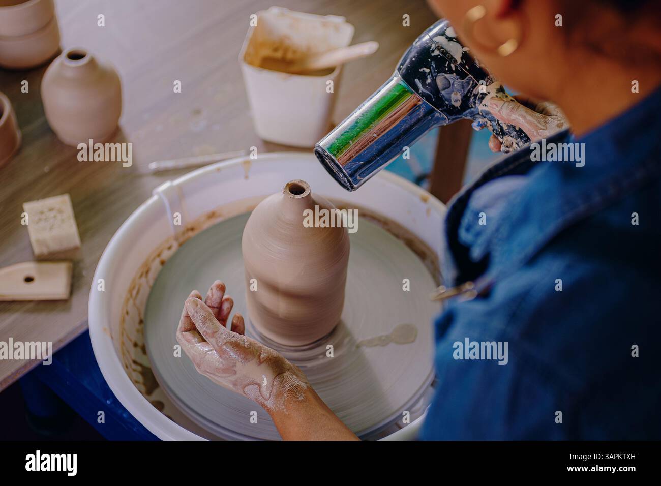 Una giovane donna messicana di 24 anni usa un asciugacapelli per asciugare un pezzo di ceramica. Il primo piano mette in evidenza la precisione e la cura che ha nelle mani durante il processo. Foto Stock