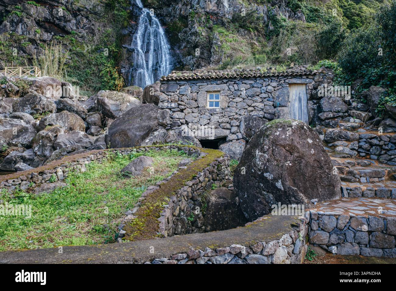 Un'affascinante casa in pietra in rovina si trova tra le rocce vicino a una splendida cascata a Sao Jorge, Azzorre, Portogallo. Una scena pittoresca Foto Stock
