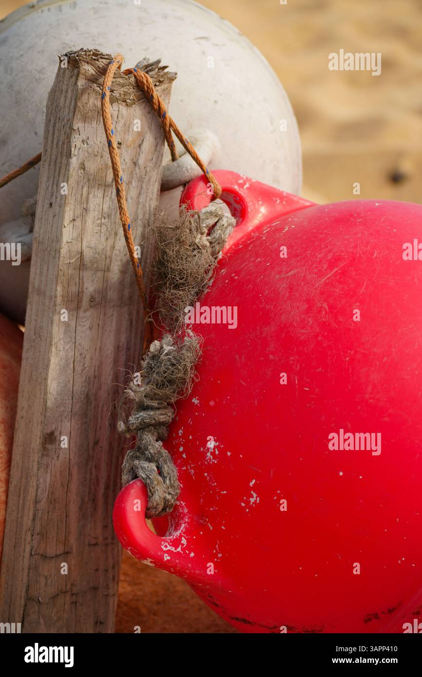 Primo piano di boe da pesca rosse e bianche legate con corda sfilacciata sulla spiaggia sabbiosa. Struttura costiera, dettagli nautici perfetti per l'industria marina Foto Stock