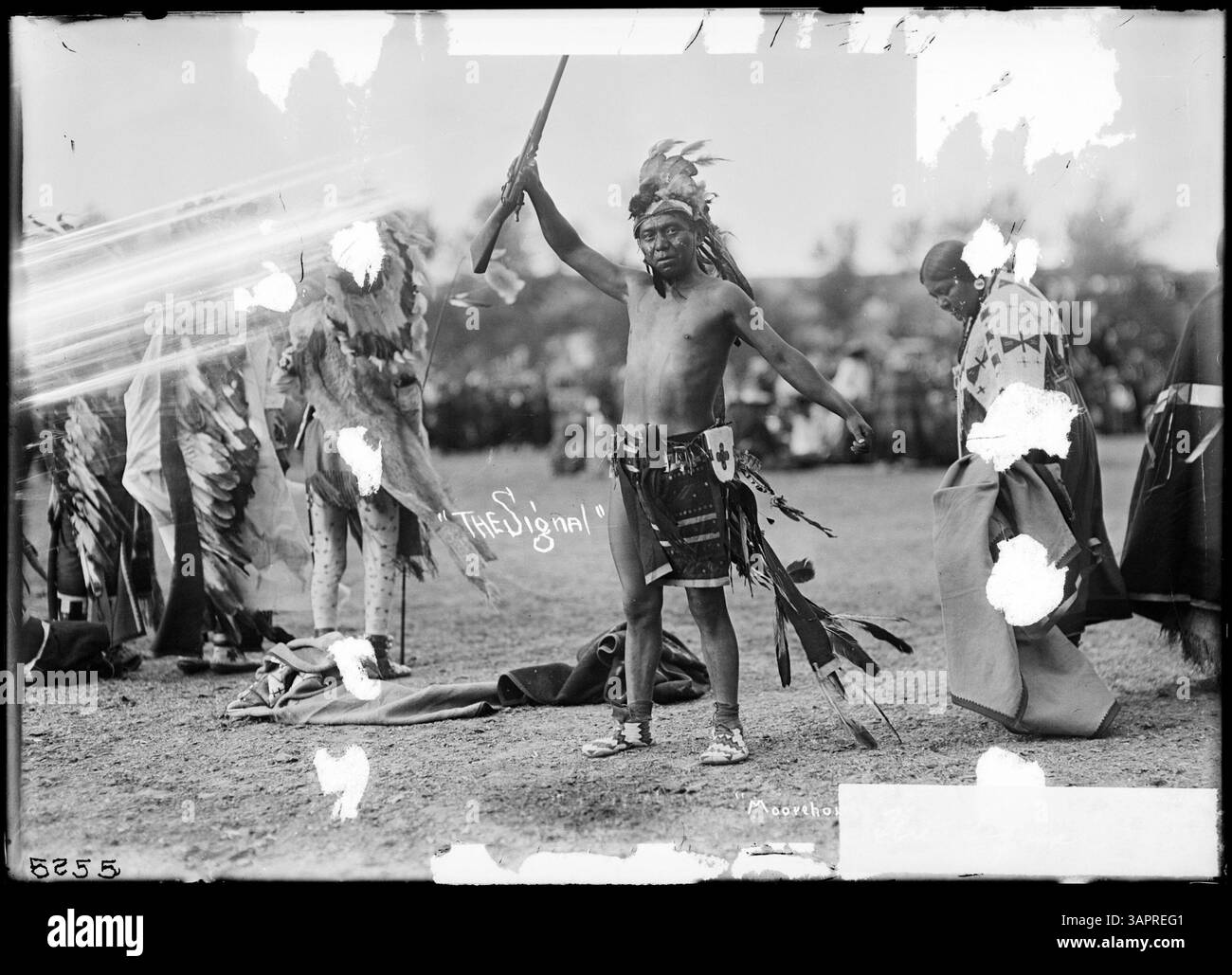 Questa fotografia mostra un indiano che tiene un fucile in una mano, con le braccia sollevate, che presenta una rappresentazione simbolica della sfida o della forza nella cultura dei nativi americani. Foto Stock