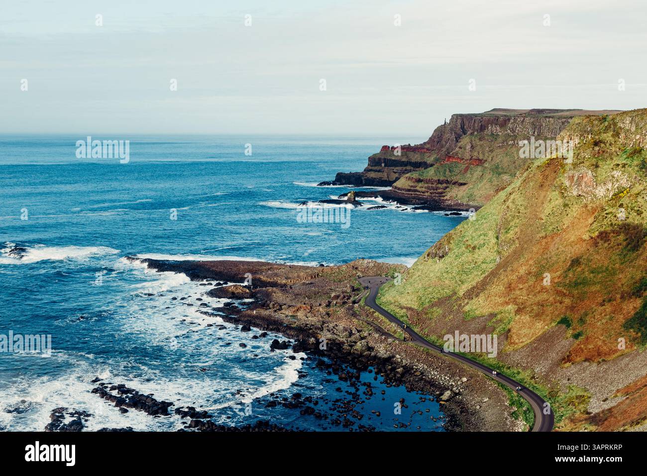 Moody Aerial View of Giant's Causeway with Waves Crashing into the Rocks and People Walking Around Foto Stock