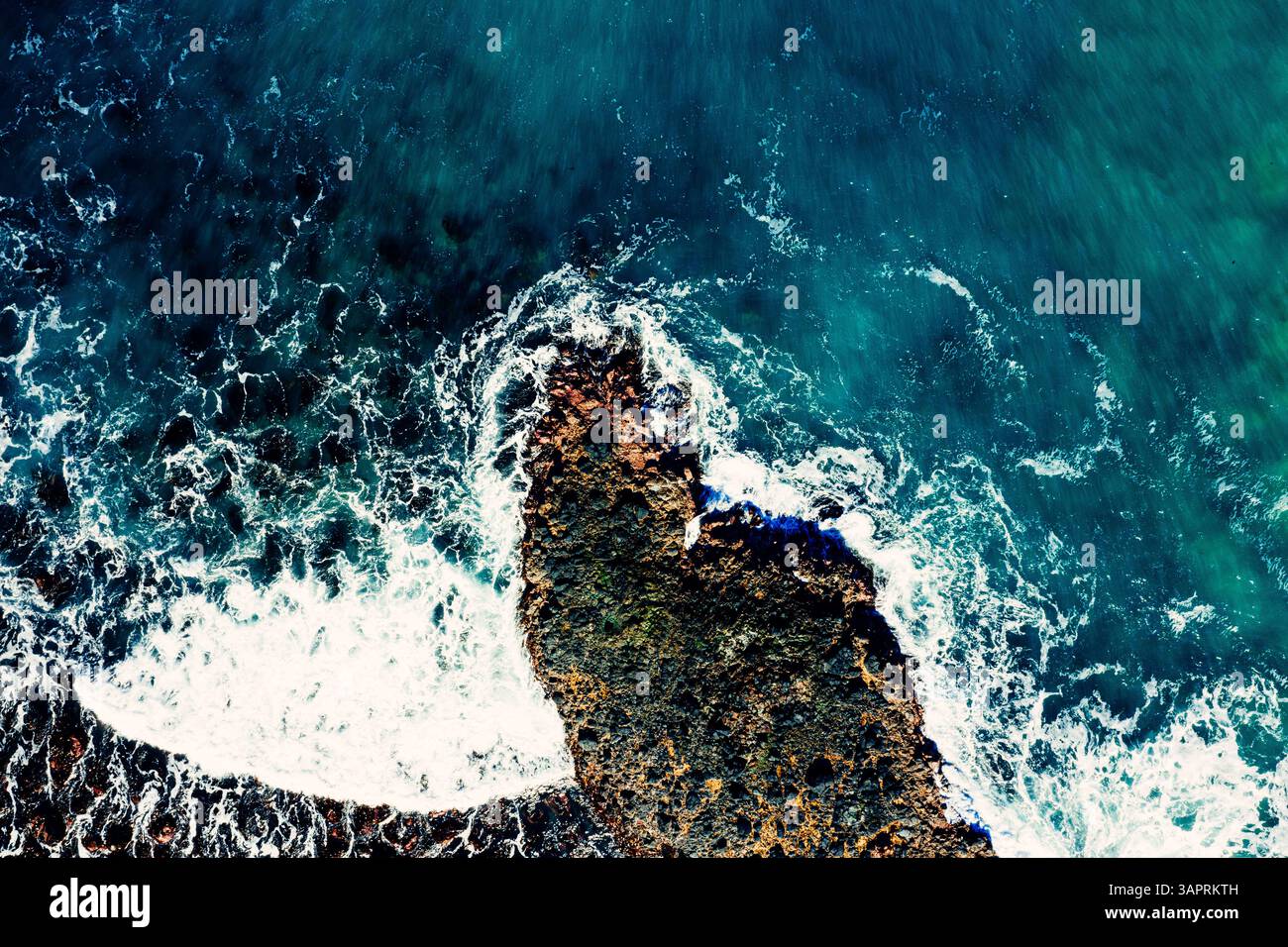 Vista dall'alto del drone sulle onde schiumose che colpiscono le rocce lungo la costa Foto Stock