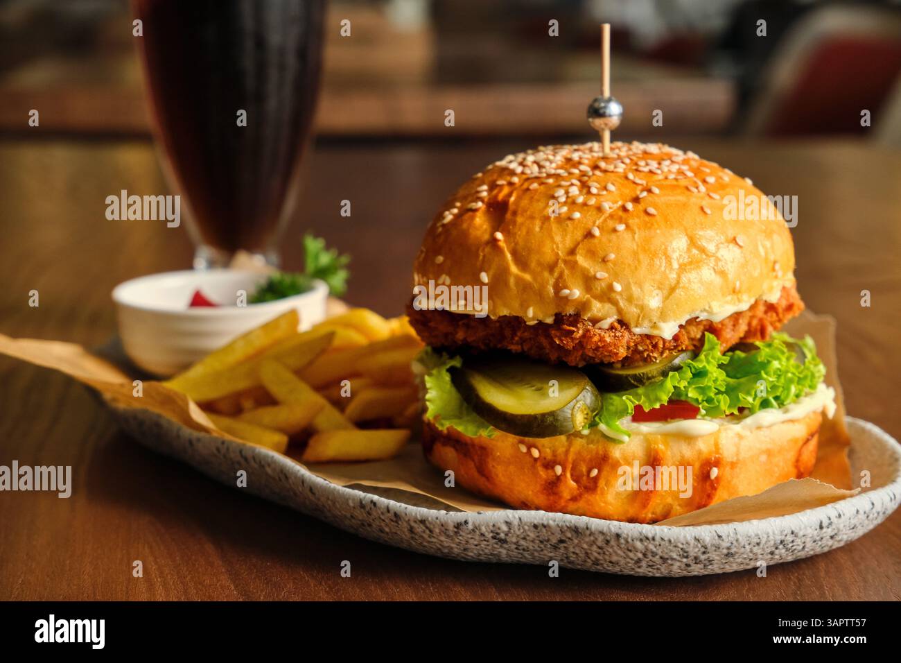 Un delizioso hamburger con patatine fritte e salsa si trova su un tavolo di legno. Un panino di sesamo, lattuga fresca, cetrioli e polpette: Una combinazione classica. Foto Stock