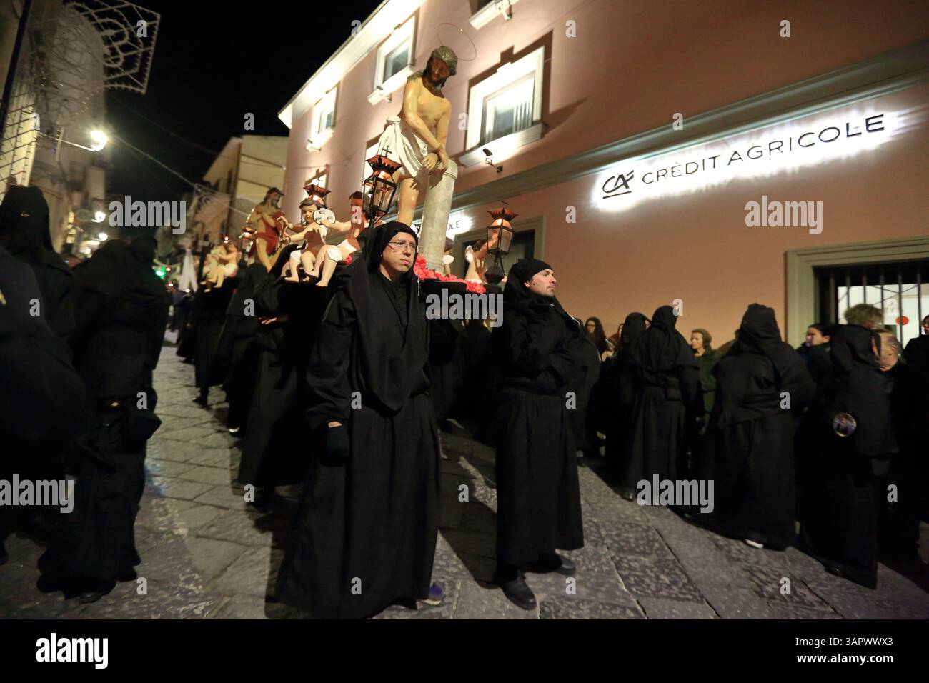 Le persone vestite di nero e con cappuccio sono in processione per le strade del centro storico la sera del venerdì della settimana Santa per celebrare i morti . Foto Stock