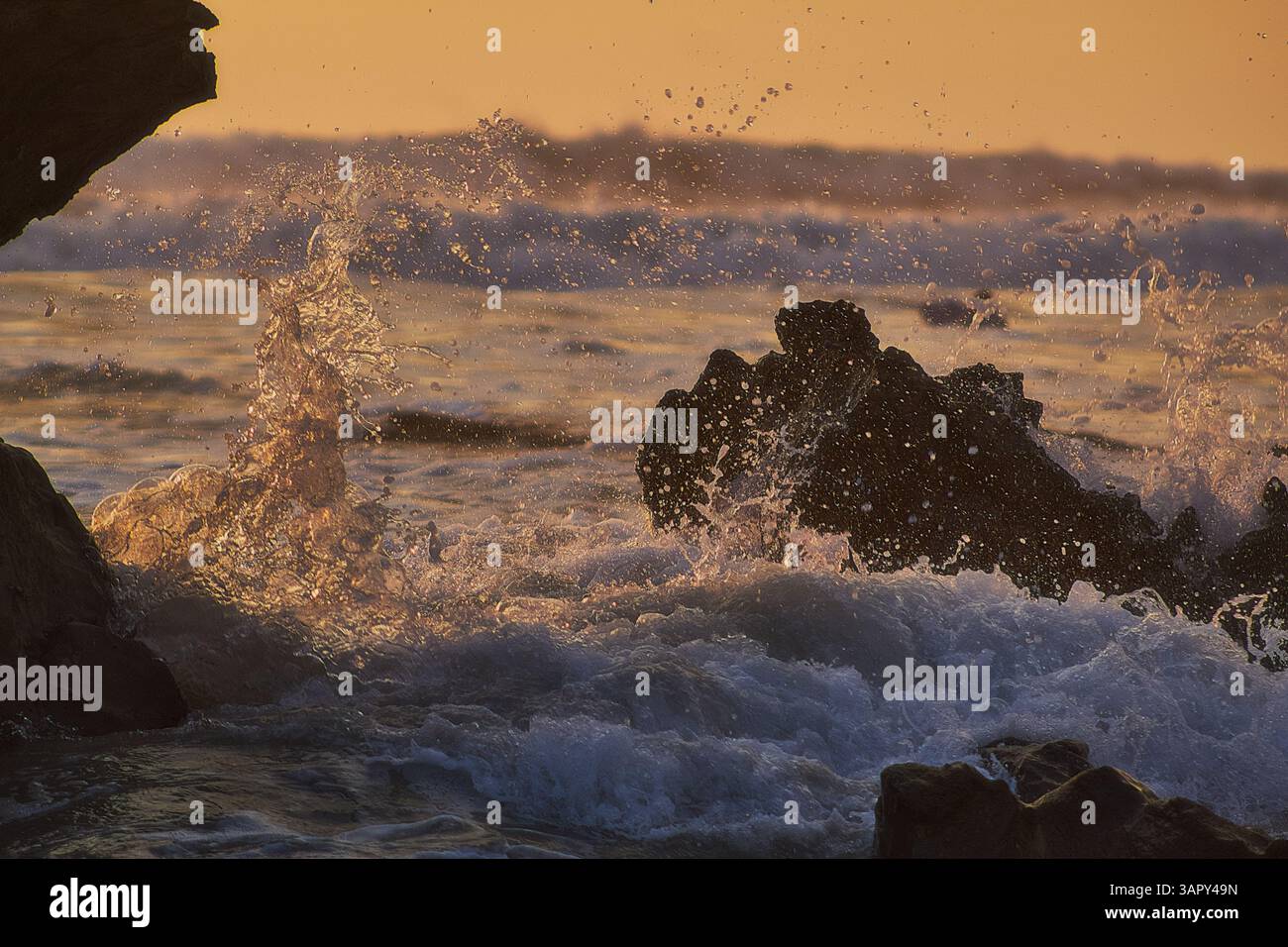 Tramonto sull'Oceano Pacifico con onde che si infrangono contro le rocce costiere, catturando la bellezza e l'energia selvaggia della costa Foto Stock