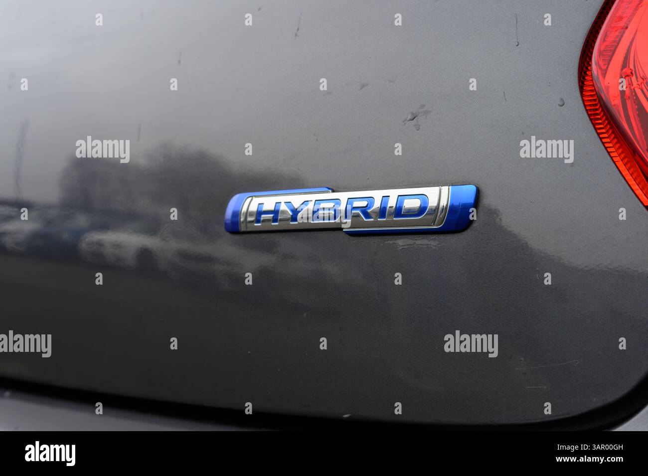 Un'auto ha un emblema blu e argento con la scritta "ibrido". L'auto è parcheggiata in un parcheggio Foto Stock