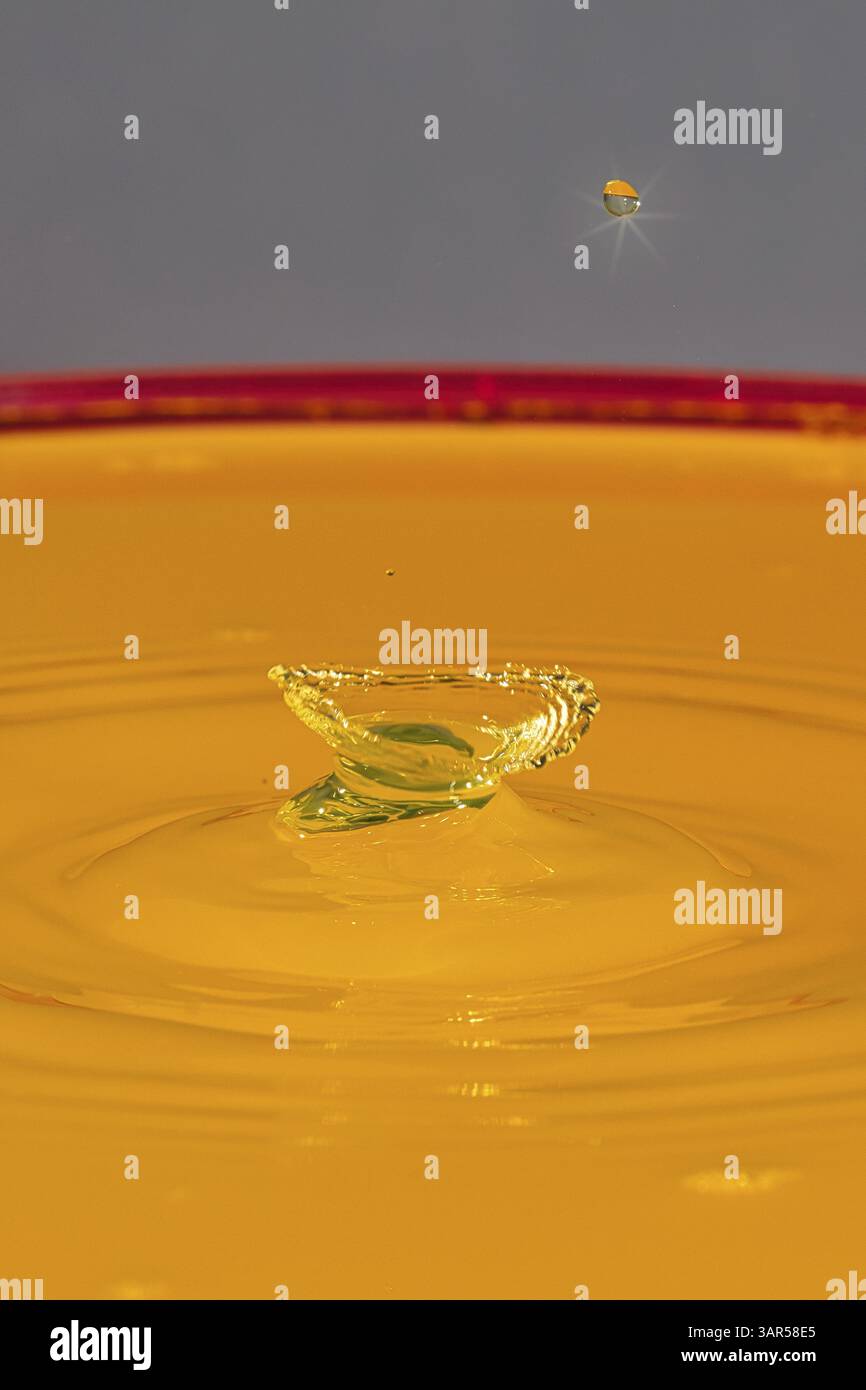 Una singola goccia d'acqua su un liquido arancione con una superficie calma, goccia d'acqua, collisione, fotografia ad alta velocità, concept Foto Stock